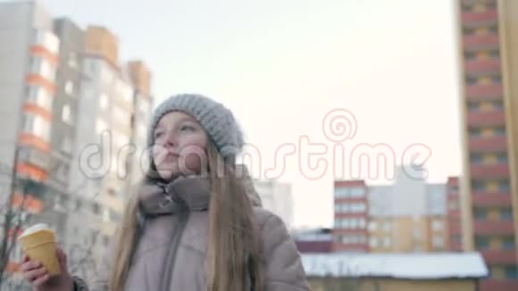 可爱的女孩在冬天吃冰淇淋在街上散步视频的预览图