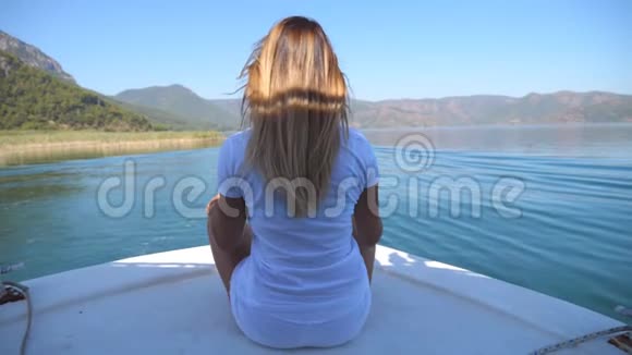 年轻女孩坐在船头在阳光明媚的日子里眺望美丽的自然景观快乐的女人视频的预览图
