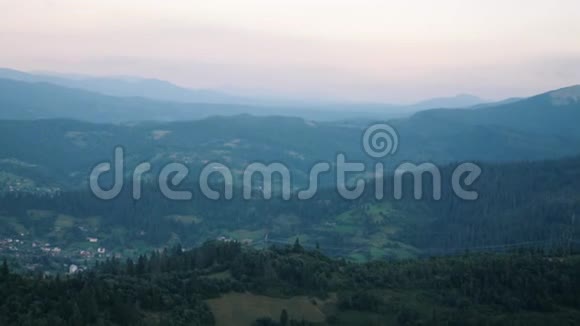 山谷中的村庄在绿松树之间黄昏时分地平线上有夕阳喀尔巴阡山脉夏季美丽的m视频的预览图