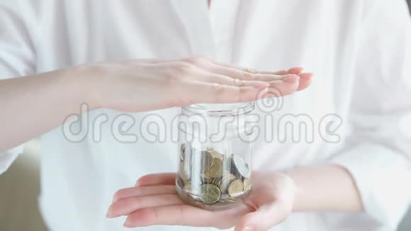 特写慢镜头视频年轻女子把硬币扔进玻璃罐存钱并摇晃视频的预览图