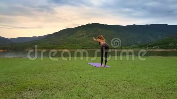 Flycam侧景女孩保持瑜伽姿势在湖边山岸视频的预览图
