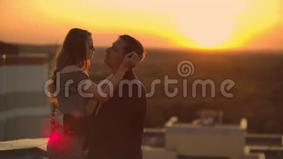 拥抱站在屋顶日落日落时的夏季屋顶一个男人和一个女孩在屋顶上进行了一次浪漫的约会视频的预览图