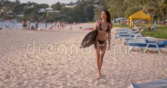 带着冲浪板在沙滩上散步的快乐女人视频的预览图
