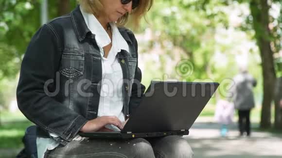 女人坐在公园里用笔记本电脑工作视频的预览图