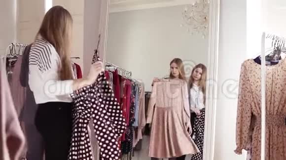 姐妹或朋友正在尝试时髦的服装同时在服装精品店或商场照镜子作出决定视频的预览图