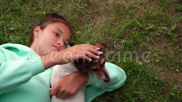 美丽的女孩躺在绿草上早上拥抱狗视频的预览图