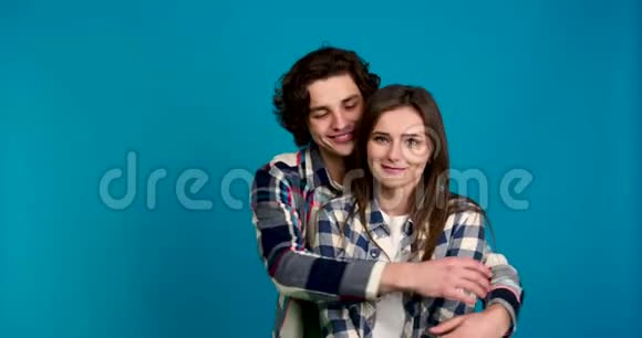 男人穿着格子衬衫微笑着拥抱亲吻女朋友蓝底隔离视频的预览图