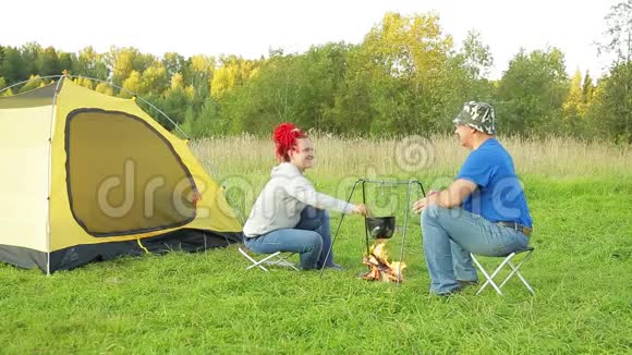 在一个阳光明媚的夜晚一对男女在靠近火的帐篷旁用锅做饭视频的预览图