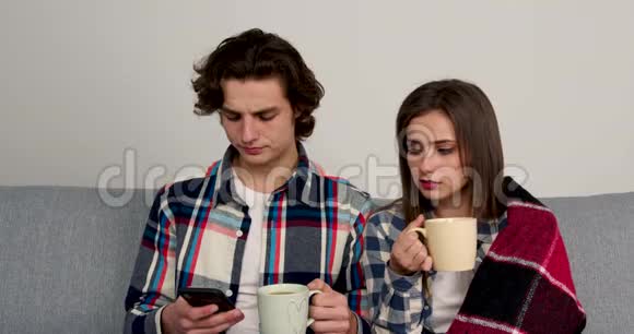 一对夫妇坐在沙发上喝茶用智能手机视频的预览图