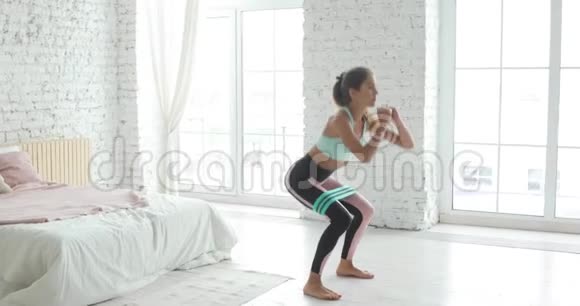 女孩正在做蹲臀部使用拉伸带锻炼训练在家里视频的预览图