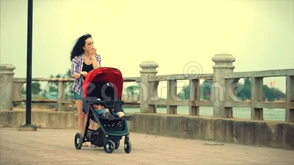 夏日里美丽的女人陪着婴儿散步年轻的母亲带着婴儿河岸边视频的预览图