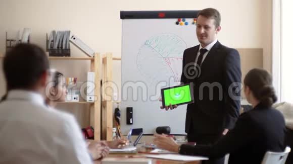 白种人穿着夹克和领带手里拿着一个绿色屏幕的平板电脑站在白板旁边拿着一个绿色屏幕视频的预览图