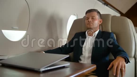 年轻企业家睡在舒适的扶手椅里坐在私人飞机里视频的预览图