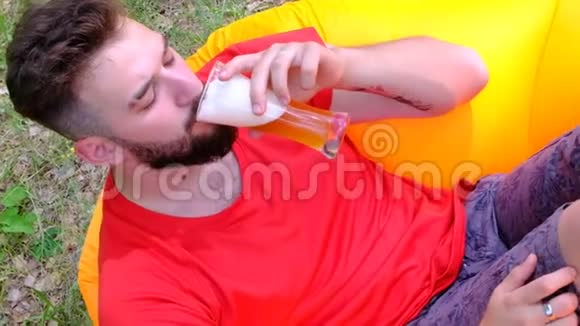 穿红色t恤的人正躺在橙色的椅子上喝啤酒一个留着胡子的年轻人视频的预览图