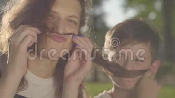 姐姐花时间和弟弟在户外的肖像男孩和女孩用头发做假胡子视频的预览图