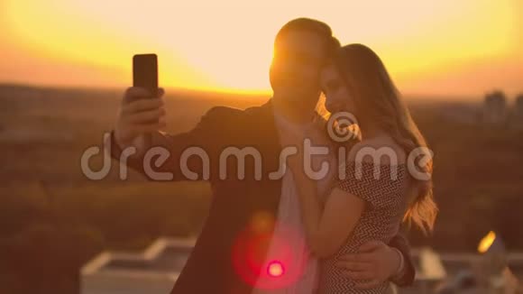 日落时分一对已婚夫妇站在屋顶上一男一女拥抱在电话上自拍拍照视频的预览图