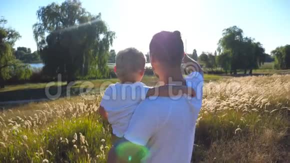 父亲和小孩在草地上挥手年轻的爸爸抱着他的儿子看大自然幸福家庭视频的预览图