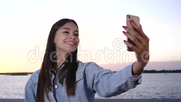 年轻迷人的女人微笑着在日落时在海滩上自拍视频的预览图