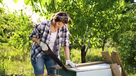 穿着格子衬衫的女木工在夏园里锯木板视频的预览图