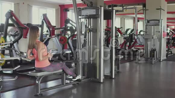 女孩在健身房或健身俱乐部的训练模拟器上摇动手臂肌肉做身体抽搐和运动的女人视频的预览图