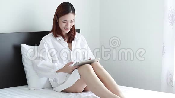 性感的女人穿着白色衬衫坐着看电脑平板上的东西开心地笑了视频的预览图
