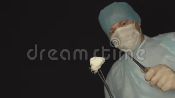 穿着镊子和医疗器械的男性外科医生在黑色背景下看相机视频的预览图