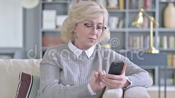 老女人庆祝沙发智能手机成功视频的预览图