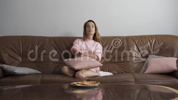 无聊可爱的年轻女人坐在棕色皮革沙发上看电视家庭主妇使用视频的预览图