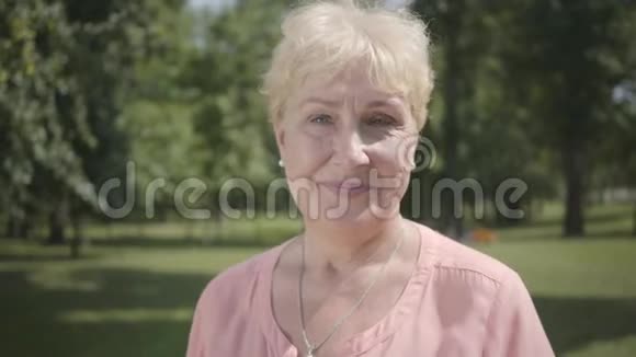 肖像老灰头发的女人看着相机站在夏季公园户外休闲成熟的白种人女士视频的预览图