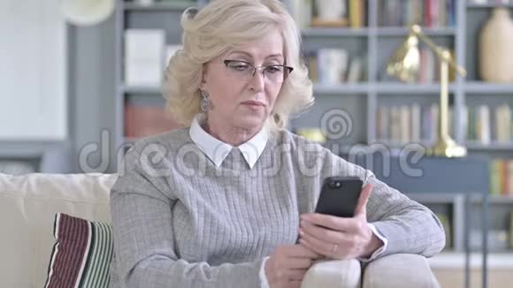 在沙发上使用智能手机的老妇人视频的预览图