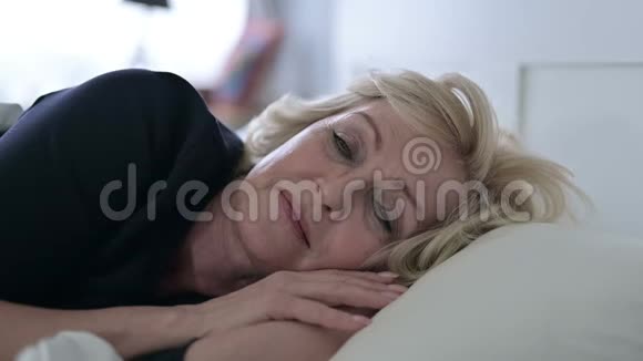 睡在床上时微笑的美丽老妇人视频的预览图