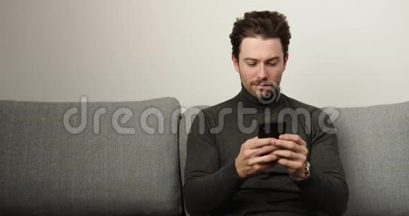 打手机短信的快乐男人聊天表现情绪坐在客厅沙发上的男人视频的预览图