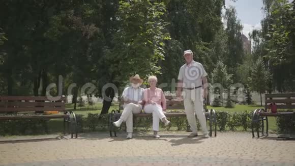 两个年长的男人和一个女人在公园里挥手成熟的人在户外休息积极的生活方式资深人士视频的预览图
