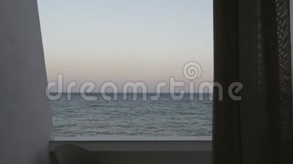 从酒店房间通过阳台到日落前大海的窗帘上观看视频的预览图