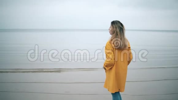 一个穿黄色外套的女人站在海岸边视频的预览图
