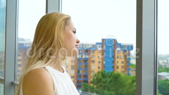从欢快的金发女人向窗外眺望城市景观视频的预览图