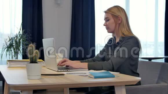 专注于工作自信的年轻女性穿着智能休闲服在笔记本电脑上工作而坐在窗户附近富有创造力视频的预览图