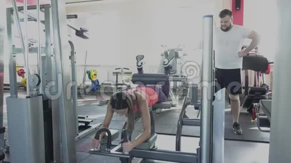 私人女教练教男人如何在健身房模拟器上做运动他的腿部肌肉会随着视频的预览图