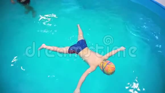 一个小男孩在游泳池里教练教他游泳俯视这个男孩屏住呼吸游泳视频的预览图