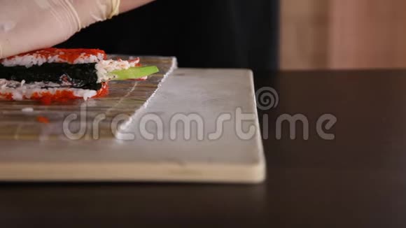 寿司制作过程的特写把寿司卷滚起来米饭诺里鳄梨螃蟹红托比科鱼子酱厨师的手竹竹视频的预览图