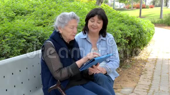 同情的看护者教这位白发苍苍的老年妇女如何在社交网络中使用平板电脑视频的预览图