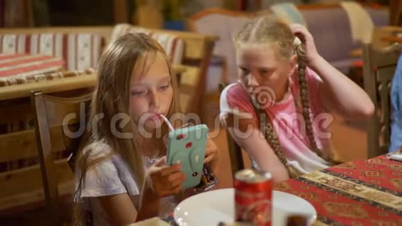 十几岁的女孩看着智能手机在吃饭年轻女孩用手机看视频两个女朋友视频的预览图