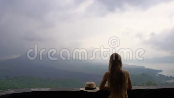 一个穿着黄色衣服和帽子的年轻女子参观了一个观点在巴图尔山上看到了一个风景它隐藏在里面的卡尔德拉视频的预览图