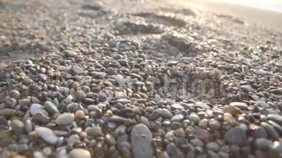摄像机沿着岩石海滩向前移动带着鹅卵石五颜六色的石头在阳光下东方日出或日落视频的预览图