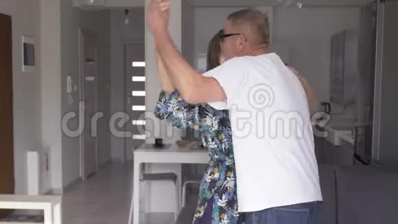 快乐的老夫妇在厨房里笑着跳舞美丽浪漫的中年老年祖父母放松视频的预览图
