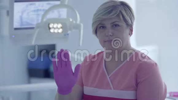 在牙科办公室的工作场所戴着医用手套的女牙医在看摄像机时会显示手势女性视频的预览图