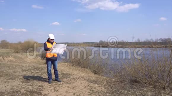 穿着信号背心和头盔的男工程师正在河的背景下看浅水计划视频的预览图