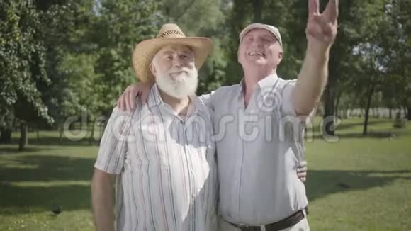 两个积极的老人望着远处邀请第三个朋友加入他们的公园户外休闲成熟的人视频的预览图