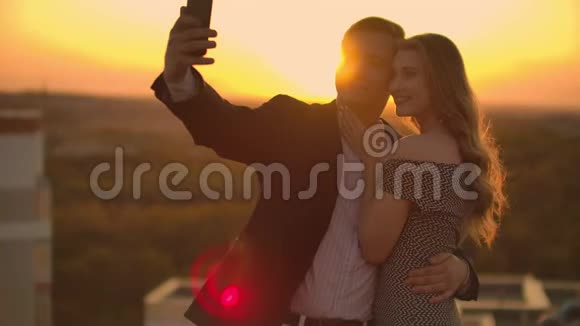 日落时分一对已婚夫妇站在屋顶上一男一女拥抱在电话上自拍拍照视频的预览图