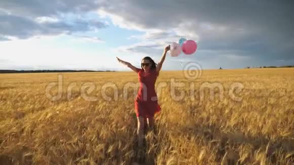 年轻的微笑的女人棕色的头发穿过金色的麦田手里拿着气球可爱的快乐女孩视频的预览图